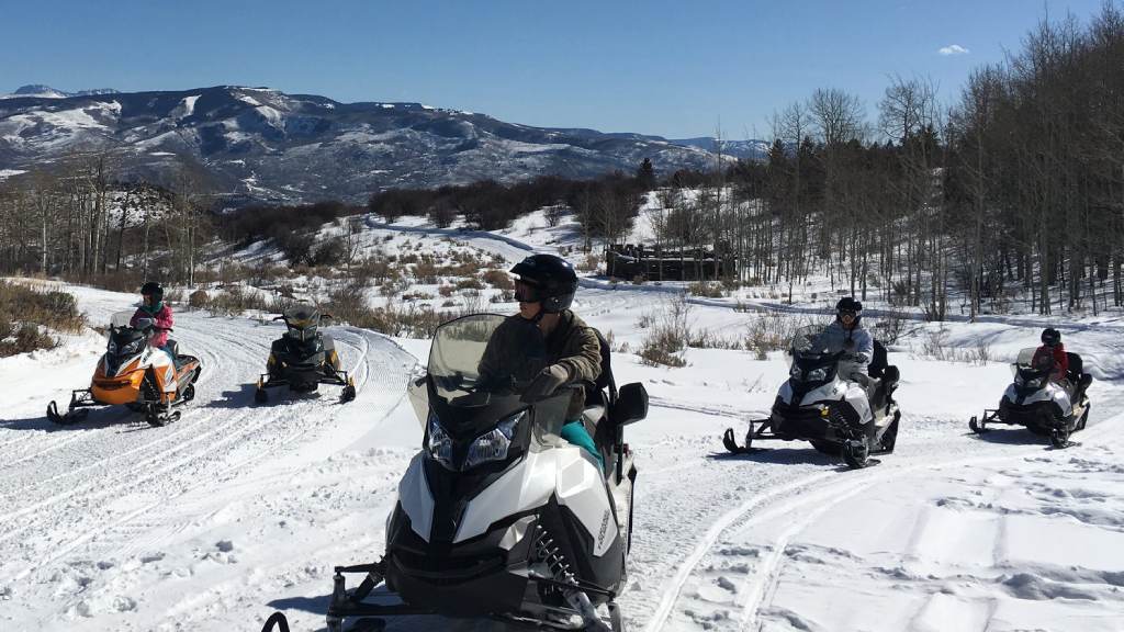 snowmobiling-group-march-featured a group of people sitting in the snow