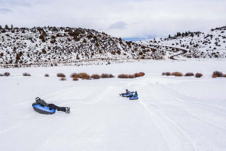 A group works their way down the slope of the tubing hills with the sage bruch mountain side in the distance.