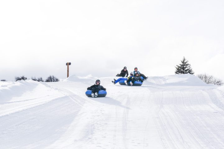 A group of people snow tube down a run at the Sage Outdor Adventures Excursion Resort near Vail. All are wearing helmets for safety.
