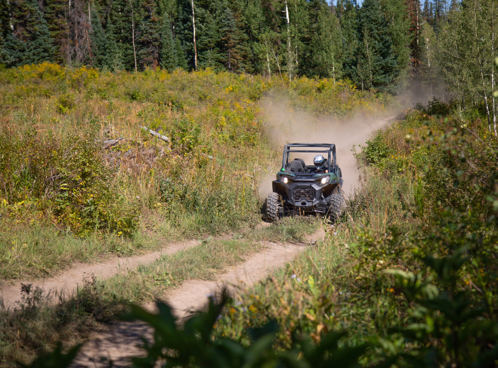 atv-vail-co ATV driving on a dirt path through a lush, green forest landscape.