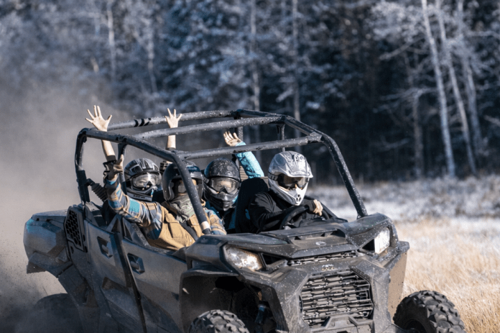 Group riding an off-road vehicle on grass with trees in background.
