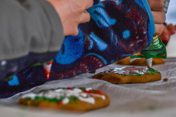 Hands decorating cookies with icing on a table.