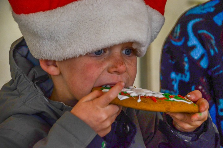 Child in Santa hat eating a decorated holiday cookie.